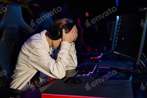 Preview: upset gamer in headphones with hands on face after a losing cybersport match, disappointment