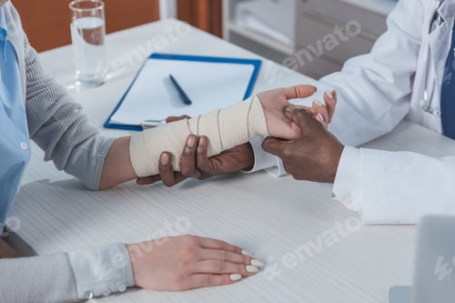 Preview: Cropped image of african american doctor examining injured hand in elastic bandage