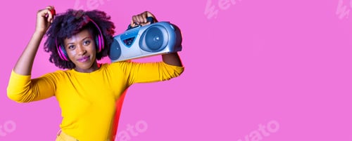 Preview: Young black woman dancing listening music wireless headphnes holding boombox isolated background