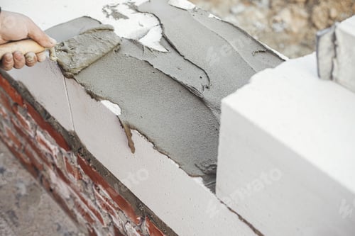 Preview: Builder installing masonry white blocks close up. Worker laying aerated concrete blocks