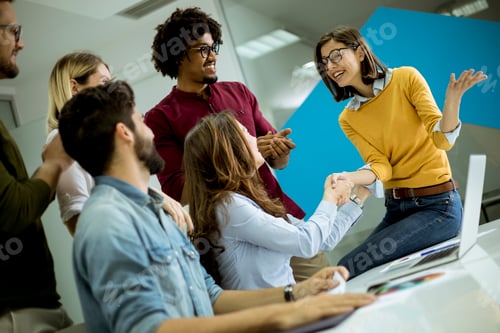 Preview: Group of young coworkers interacting around a table and handshaking in the office