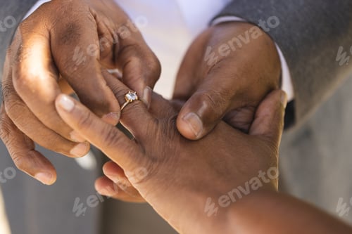 Preview: Hands of senior biracial groom putting wedding ring on finger of his bride