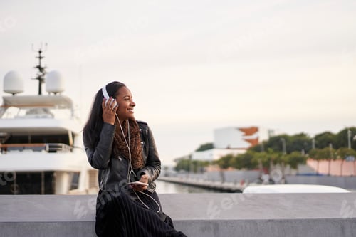 Preview: Portrait of young African American woman with headphones listening to music outdoors