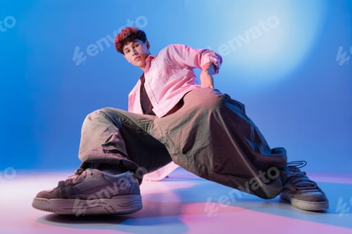 Preview: Low-angle Bboy in streetwear posing in studio with blue neon lighting