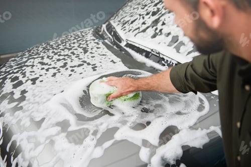 Preview: cropped image of man cleaning car at car wash with rag and foam