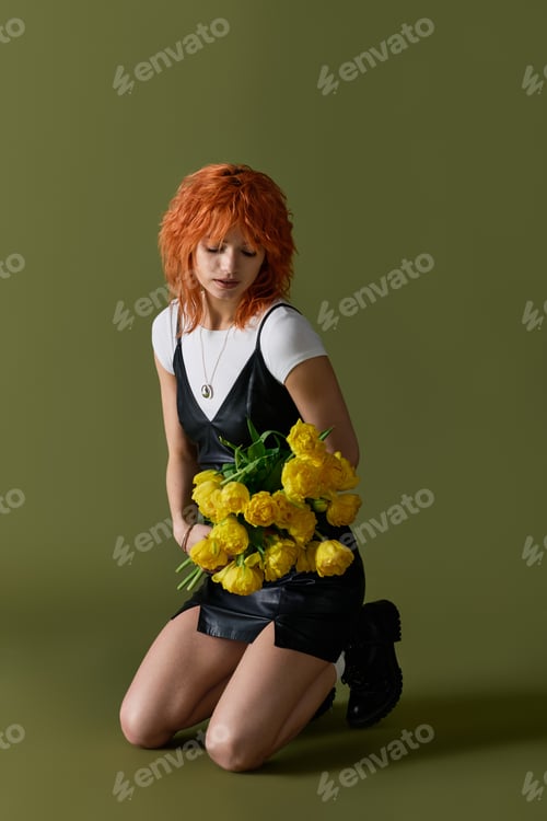 Preview: Young redhead woman poses gracefully with yellow flowers in a stylish spring outfit