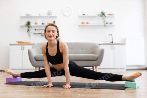 Preview: Woman practicing yoga splits indoors on yoga mat
