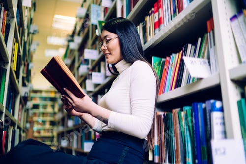 Preview: Cheerful woman reading book in library