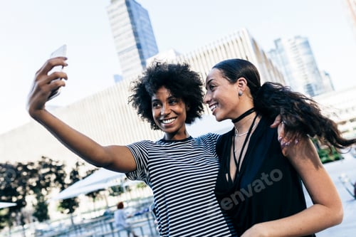 Preview: USA, New York City, two happy young women taking selfie with smartphone
