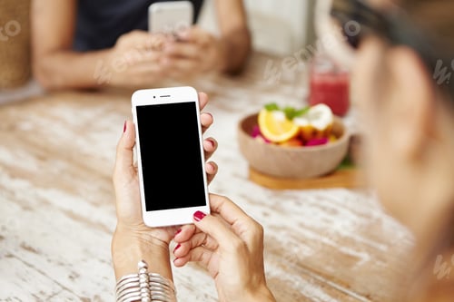 Preview: Cropped view of female hands with red manicure holding cell phone with blank screen. Woman using ele