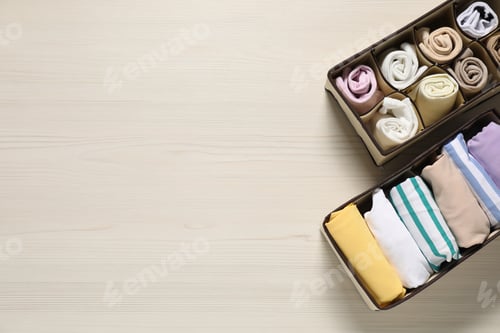 Preview: Organizers with folded clothes on light wooden table, flat lay. Space for text