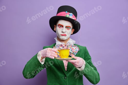 Preview: Bored displeased man hatter obsessed with drinking tea wears big hat green costume bowtie poses agai
