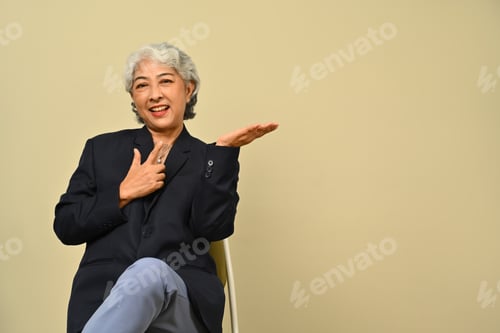 Preview: Smiling senior businesswoman wearing black suit pointing aside.