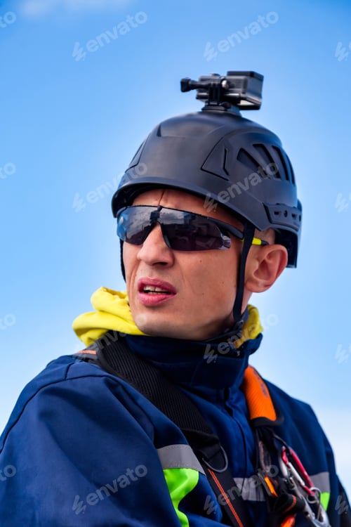 Preview: Portrait of industrial mountaineering worker in uniform helmet sunglasses at blue sky background