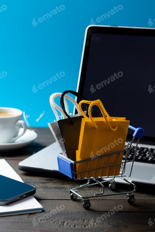 Preview: Composition of shopping cart with bags and laptop on blue background