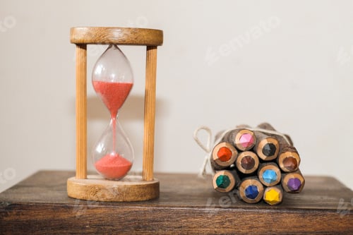 Preview: Colorful pencils and an hourglass on the table.