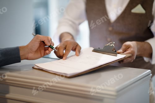 Preview: Man Signing Papers Checking In At Hotel Reception Indoors, Cropped