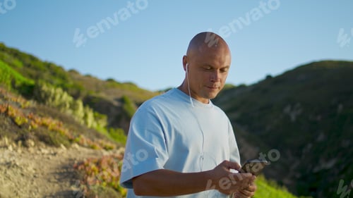Preview: Happy guy hold smartphone in mountains evening. Smiling muscular man enjoying