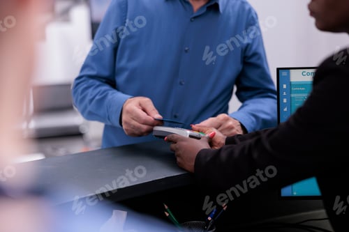 Preview: Elderly patient standing at registration counter paying with credit card for medication treatment