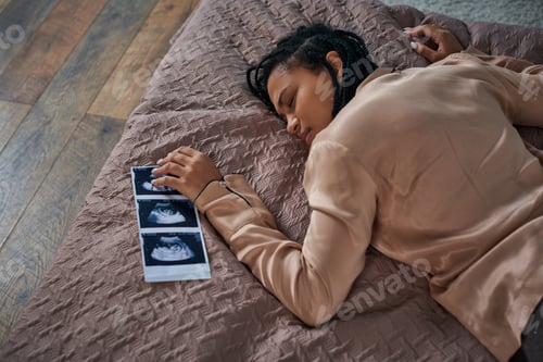 Preview: top view of worried african american woman lying on bed near ultrasound, unborn baby, abortion