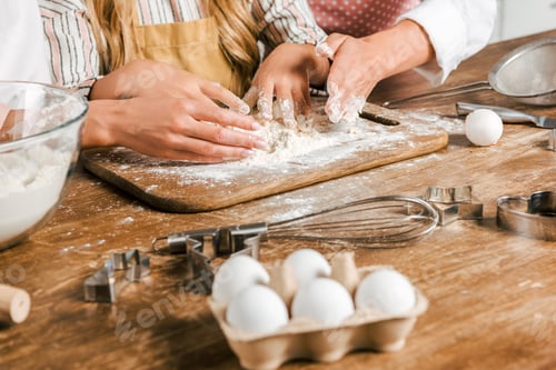 Preview: cropped shot of kid and women making dough together on wooden board