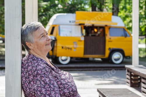 Preview: portrait senior woman relaxing at park on yellow mini van background during sunny day