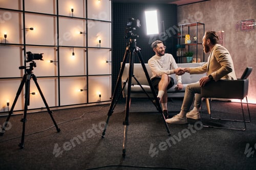 Preview: handsome elegant men with beards in chic attires shaking their hands during interview in studio