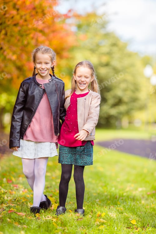 Preview: Little adorable girls at warm day in autumn park outdoors