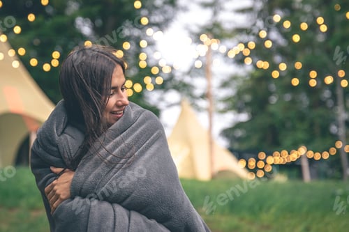 Preview: A young woman wrapped in a blanket in the forest on a blurred background.