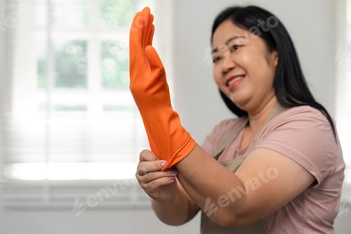 Preview: Preparing for Cleaning Tasks. A woman puts on rubber gloves with a smile in her home.