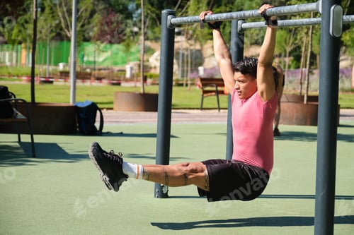 Preview: Young man performing leg raises on outdoor gym bars