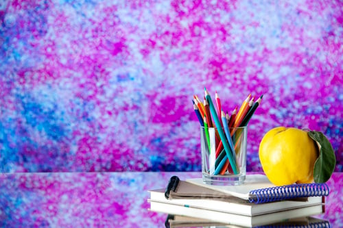 Preview: Side view of colored pencils kept in a glass jar and quince with stem on stacked spiral notebooks on