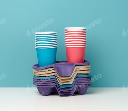 Preview: Stack of paper disposable multi-colored cups and stand on white table, blue background