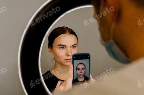 Preview: Doctor takes photo before lip augmentation for attractive girl. Cosmetic facial treatment.