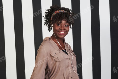Preview: Smiled afro american girl stands in the studio with vertical white and black lines at background