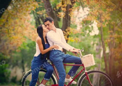 Preview: photo of cute couple sitting on bicycle and kissing on the wonderful autumn park background