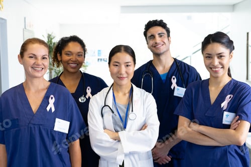 Preview: Portrait of diverse group of healthcare workers wearing cancer ribbons smiling in hospital corridor