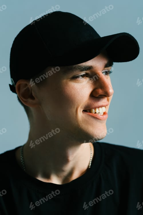 Preview: Portrait of stylish handsome caucasian man fashion model in t shirt and cap, studio shot.
