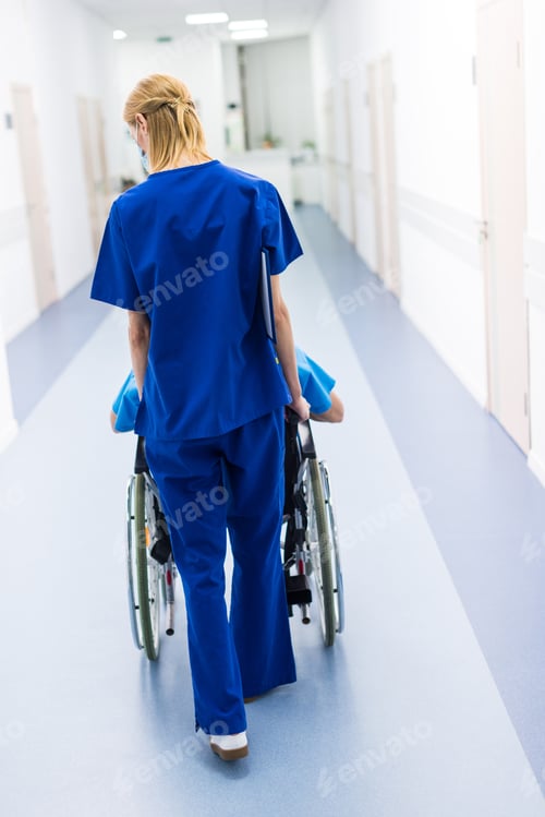 Preview: rear view of surgeon and upset patient in wheelchair in hospital corridor