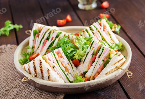 Preview: Club sandwich with ham, tomato, cucumber, cheese, and arugula on wooden background.