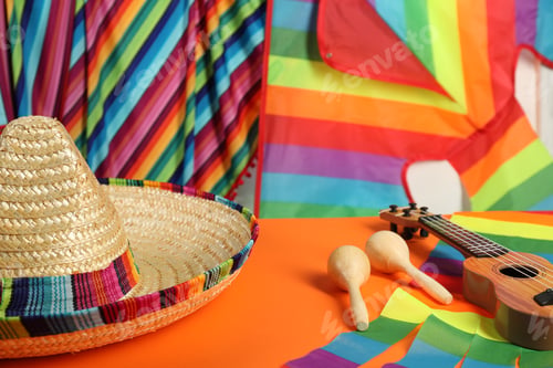 Vista previa: Mexican sombrero hat, ukulele and maracas on orange table, closeup
