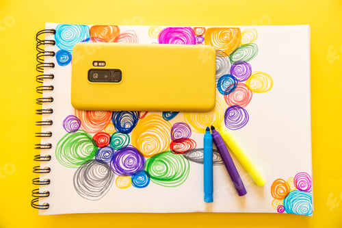 Preview: Top view of a modern yellow mobile phone on a drawing of colorful spirals with markers