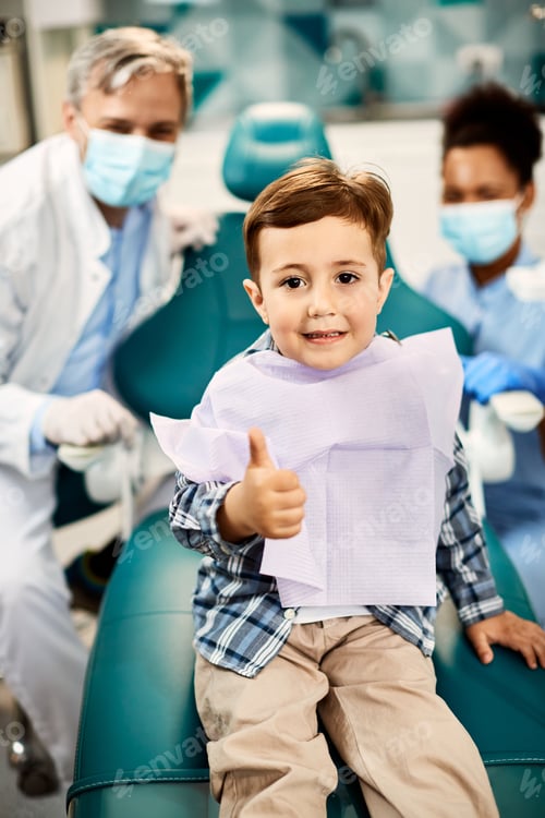 Preview: Cute kid showing thumb up while sitting on dentist's chair and looking at camera.