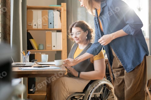 Preview: Young businesswoman in casualwear putting cup of tea for her disable colleague