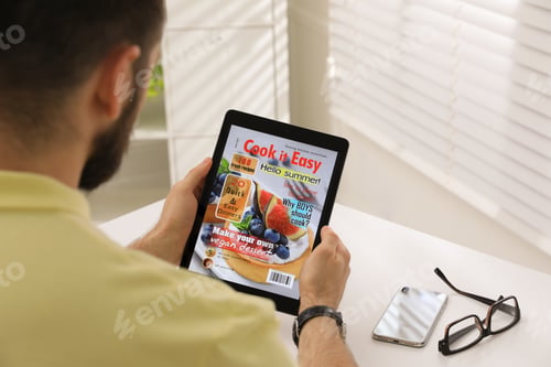 Preview: Man reading online magazine on tablet at white table, closeup