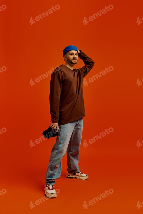 Preview: Handsome young man poses confidently against a vibrant orange backdrop in casual attire