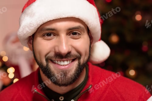 Preview: close-up portrait of handsome bearded man in santa hat smiling at camera