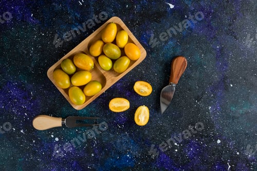 Preview: Pile of kumquats on wooden plate whole or half cut
