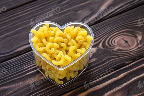 Preview: Raw pasta on dark wooden planks background. Laconic design. Symbol of love. Minimalist style. Yellow