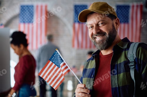 Preview: Happy US citizen with national flag at polling place on election day looking at camera.